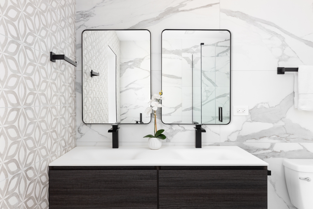 Bathroom: A Place for Texture and Tone | R&D Marble, Inc. A bathroom detail with a modern wood cabinet, pattern and marble tiled walls, a white sink and black faucets, and black framed mirrors.