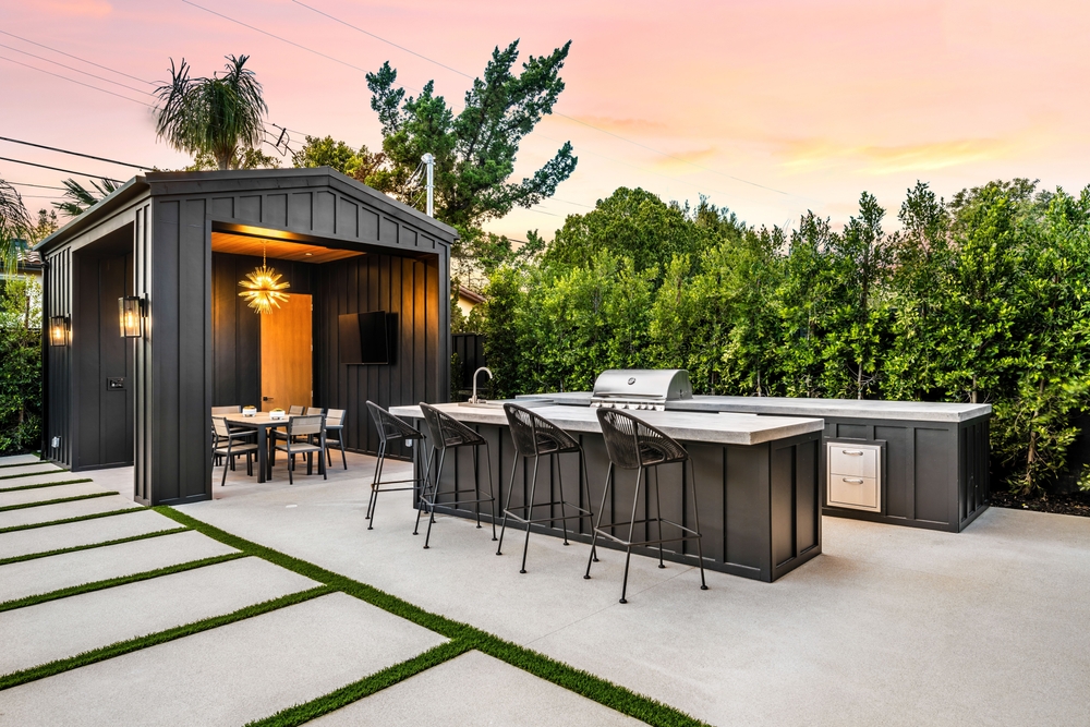 Outdoor Living: Balance Nature with Style | R&D Marble, Inc. Modern outdoor kitchen and dining area with sleek black furniture and a stylish pergola, set against a lush green garden at sunset.