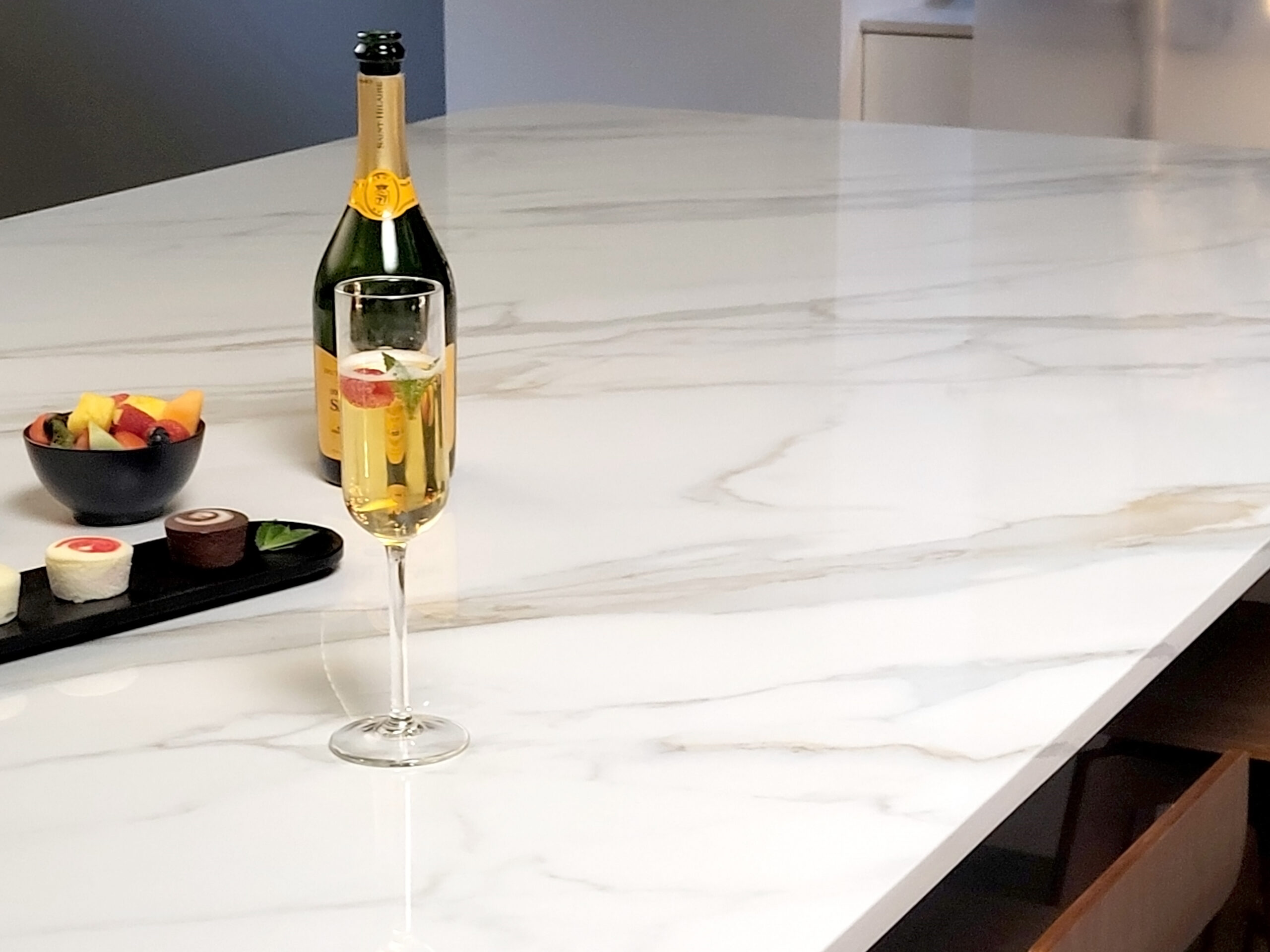 Chips, Cracks, and Other Wear and Tear | R&D Marble, Inc. Close up of champagne glass and bottle on kitchen counter made with TERACANTO porcelain in the shade Calacatta.