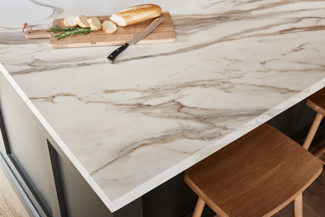 The Best Porcelain Countertop Edge for Your Remodel Closeup of the corner of a white and gold porcelain countertop edge with a plate of bread and knife on it.
