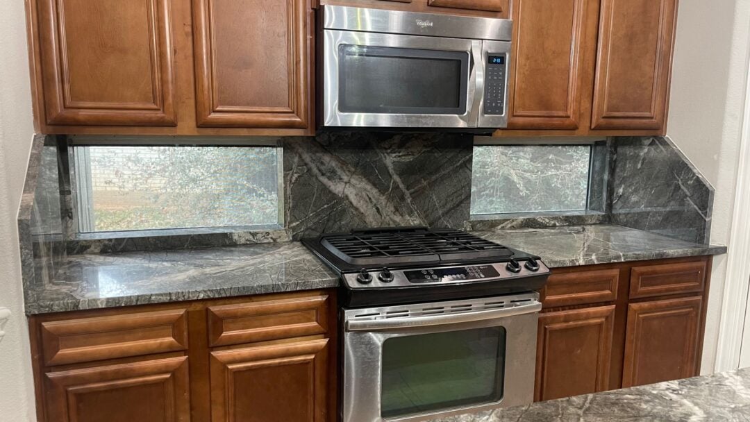 | R&D Marble, Inc. Interior of a kitchen's over and stove area with a dark quartzite backsplash and countertops.