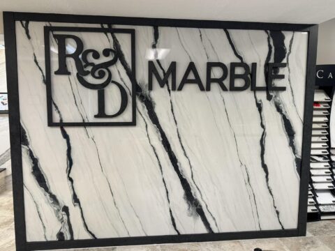 | R&D Marble, Inc. A commercial office porcelain slab wall with the R&D Marble logo on it.