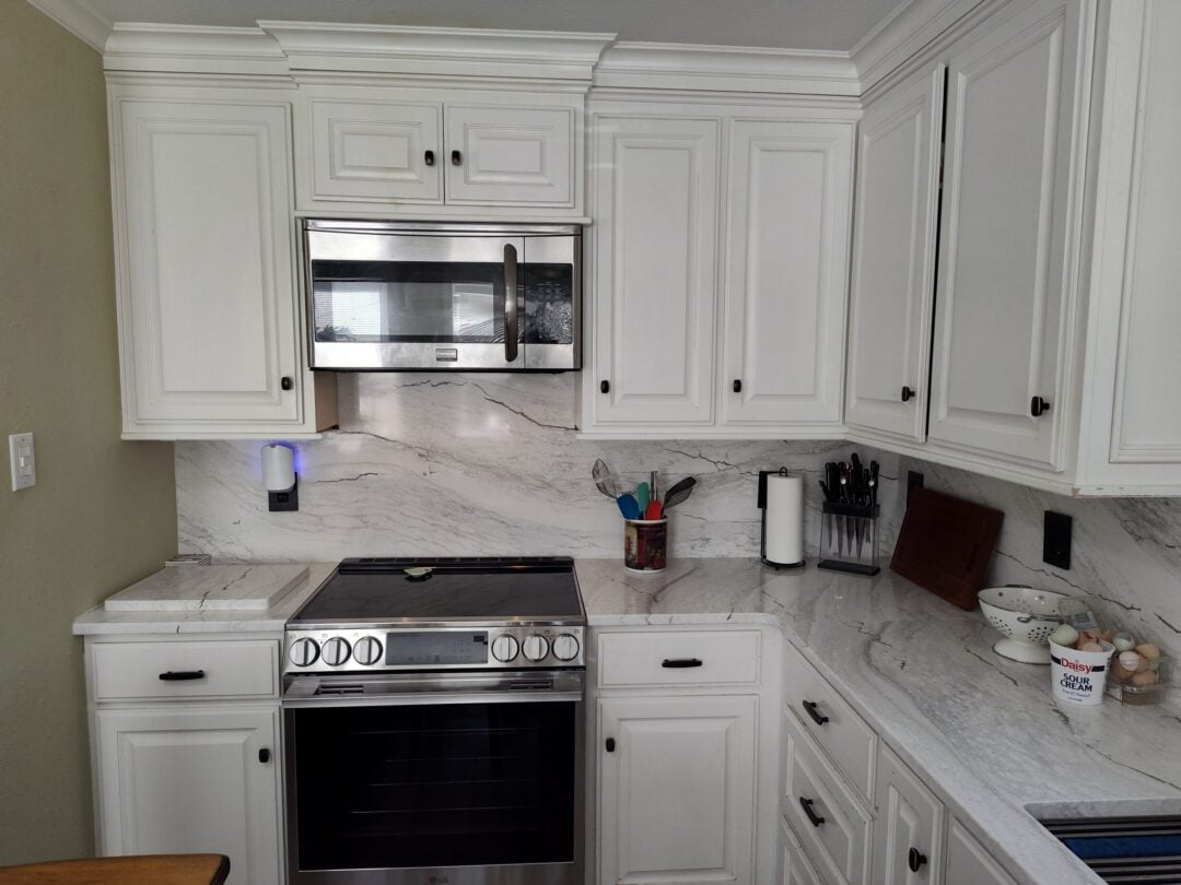 7 Oven Backsplash Ideas with Stone Slabs for Your Kitchen A newly renovated kitchen with white cabinetry and custom stone countertops and matching backsplash installed.