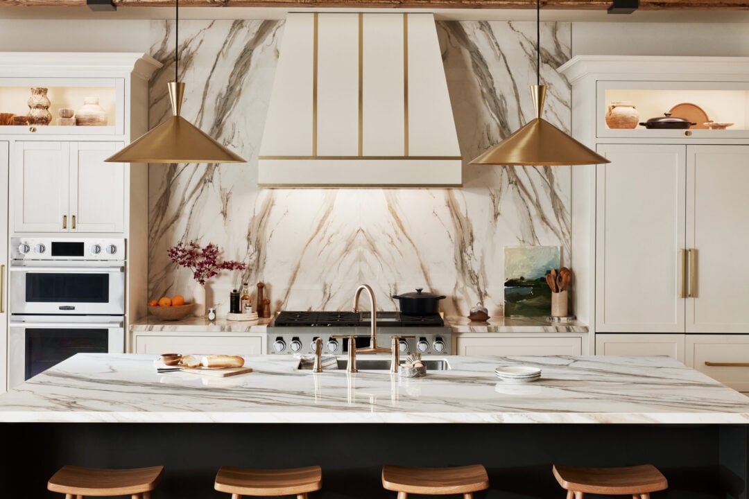 | R&D Marble, Inc. A luxurious kitchen with a bookmatched stone slab backsplash with white and gold elements.