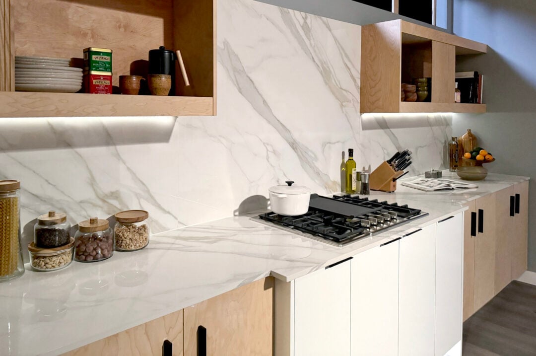 | R&D Marble, Inc. Neutral toned kitchen with white porcelain countertops and full height backsplash behind stove.