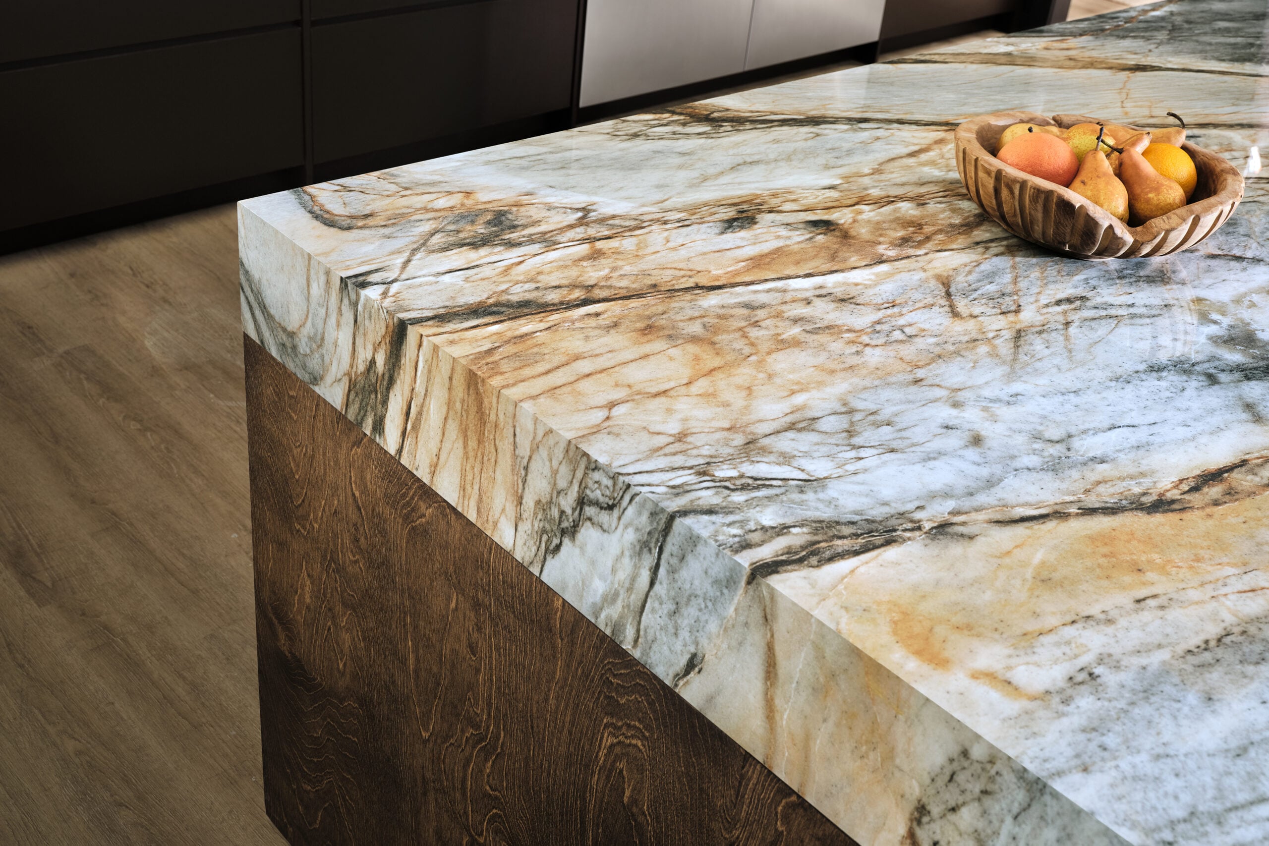 | R&D Marble, Inc. Closeup of the edge of an earth toned kitchen island with a fruit bowl on it.