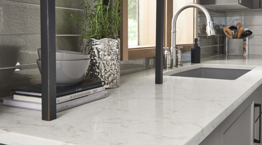 How to Style a Kitchen Counter for a Chic Look Close up of the corner of a beautiful white quartz kitchen countertop with a sink in the background and modern decor on the counter.