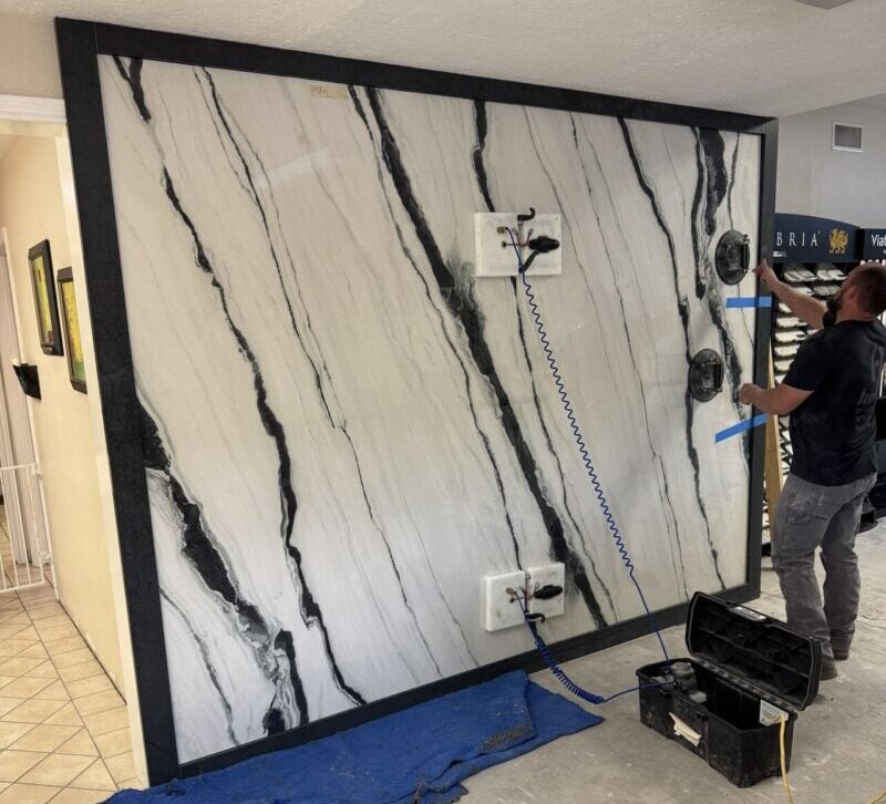 Charcoal White TERACANTO Porcelain by R&D Marble | R&D Marble, Inc. Man installs a large white marble-patterned wall panel in a showroom; blue coiled cord and tool box nearby.