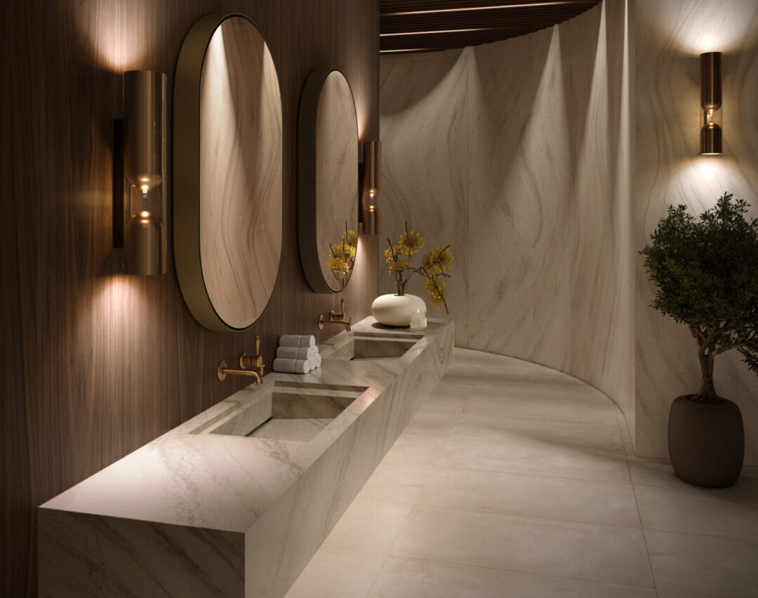 everleigh-warm-bathroom-dodd-001-24 | R&D Marble, Inc. Row of circular mirrors mounted on a dark wood wall above marble sinks with gold fixtures and warm lighting.