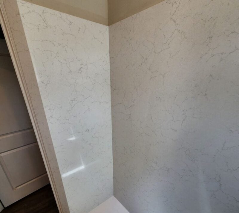 | R&D Marble, Inc. Corner interior showing white marble-patterned wall panels meeting a white staircase with dark wood flooring nearby.