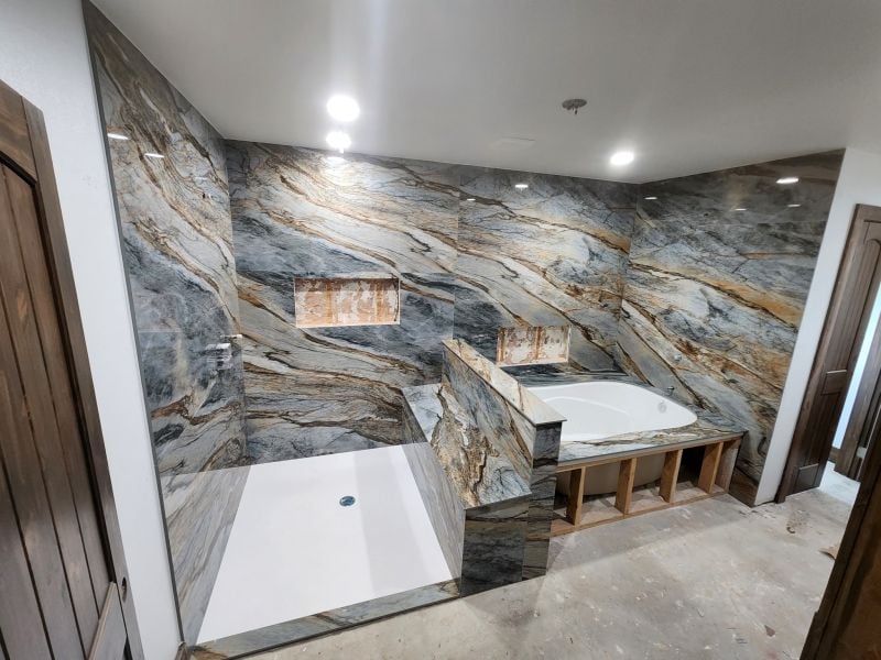 | R&D Marble, Inc. Marble-clad bathroom under construction with a corner shower, tub surround, and open wooden storage beneath the tub.
