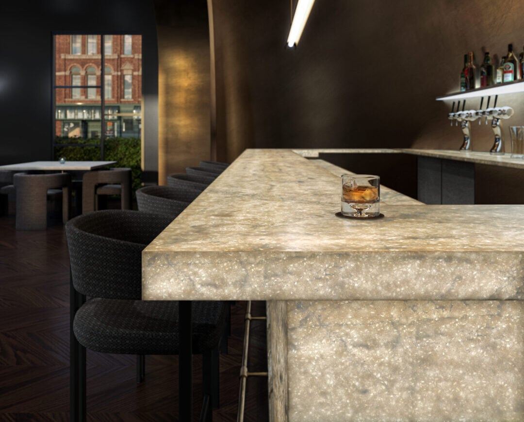 Interior of a modern bar with a speckled stone counter, dark walls, and barstools; bottles line a shelf to the right.
