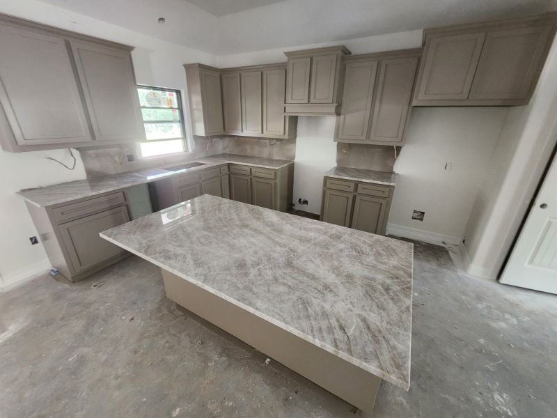 | R&D Marble, Inc. Kitchen under construction with taupe cabinets, marble-like countertops, and a large central island.