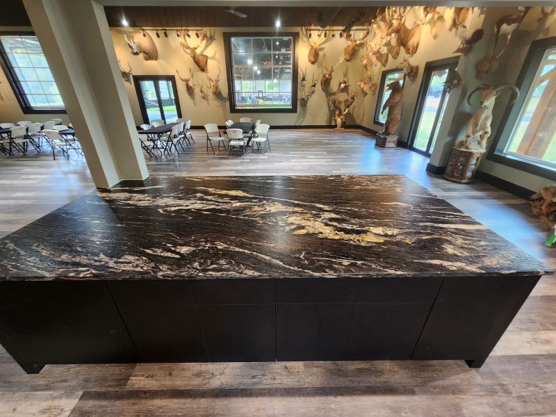 Granite Finishes Explained: Polished, Honed, and More Large dark marble-topped island in a spacious room with deer mounts on the walls and dining tables in the background.
