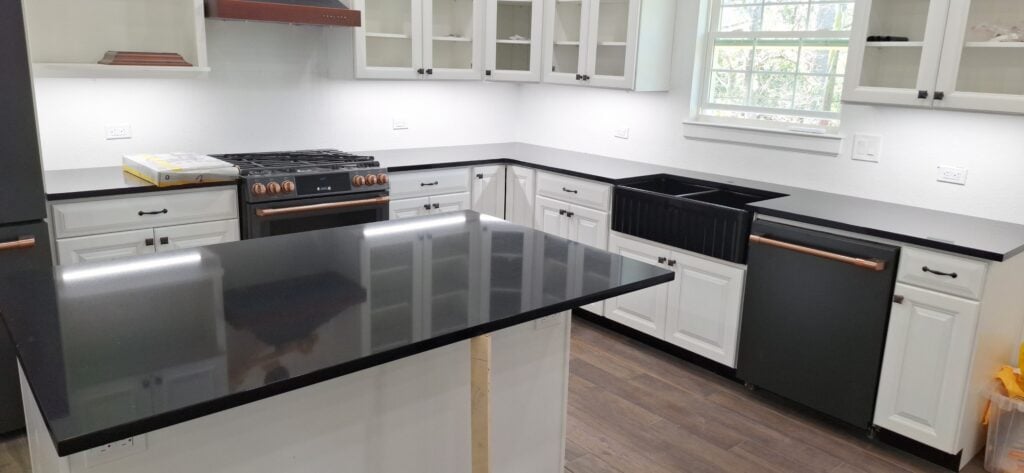 | R&D Marble, Inc. Modern U-shaped kitchen with white cabinets, black countertops, and a dark island in the foreground.