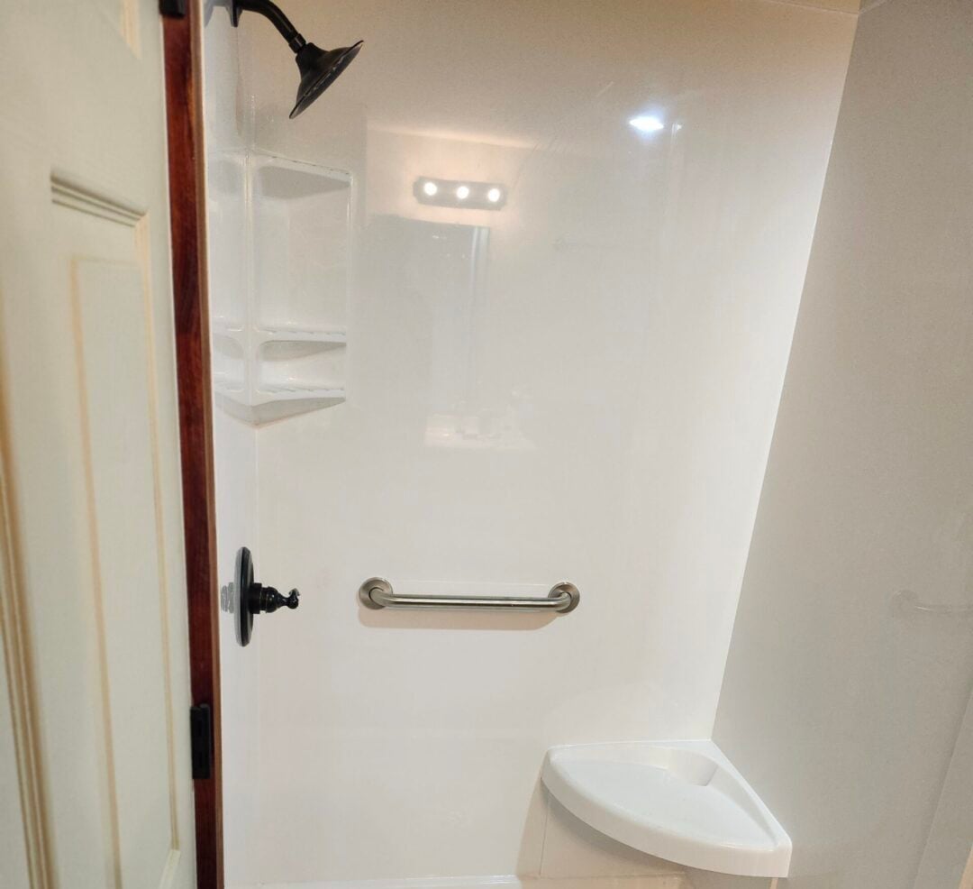 How Do You Clean a Cultured Marble Shower Walk-in shower with white acrylic walls, a chrome grab bar, and a small built-in shelf near the corner.