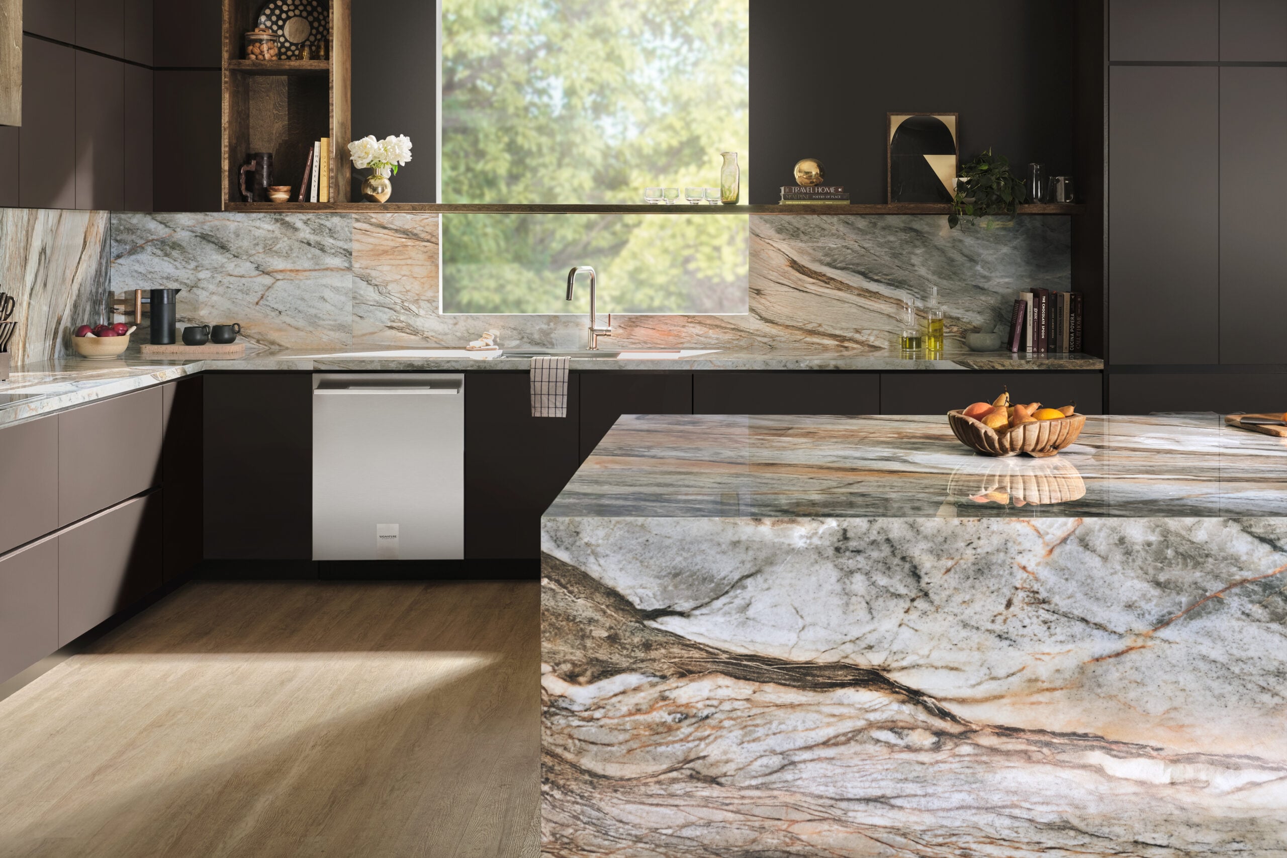 TERACANTO-Residential-Asgard-kitchen-Mid1 Modern kitchen with marble countertops, dark cabinetry, and a large island; greenery visible through a window.