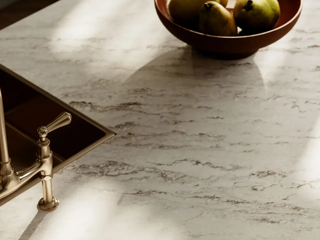 Bowl of pears on a marble kitchen counter with a nearby gold-toned faucet light and shadows.