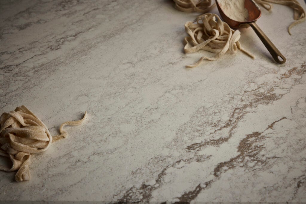 Uncooked pasta nests on a light marble surface with a metal scoop of flour nearby, ready for cooking.